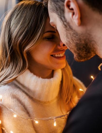 Coppia romantica con luci soffuse, sorrisi e intimità.