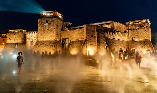 Beleuchtete Burg bei Nacht mit Nebeleffekten und Menschen in Bewegung.