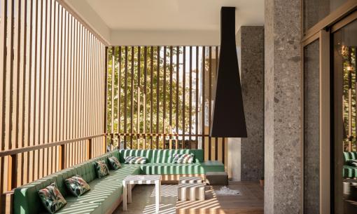 Terrasse élégante avec canapés verts, cheminée et murs en bois.