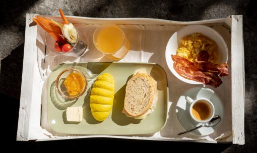 Colazione con pane, uova strapazzate, pancetta, verdure, succo d'arancia e caffè.